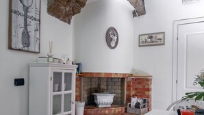 Una cocina con un arco de piedra rústica, un armario blanco, una chimenea de ladrillo y una mesa de comedor con una copa de bebida roja.