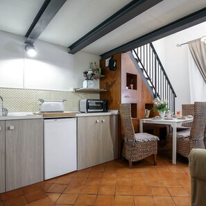 A compact kitchen with a microwave, toaster, and sink. There's a dining area with wicker chairs and a small table. A staircase leads to an upper level. - Corte Segreta Apartments (Salerno)