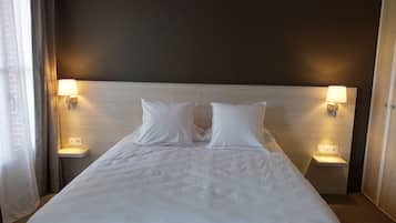 Une chambre d’hôtel avec un grand lit, deux lampes de chevet et une tête de lit sobre.