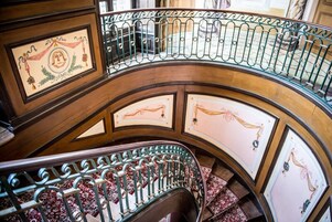Una escalera curva con barandillas de metal ornamentadas y paneles de pared con diseños.