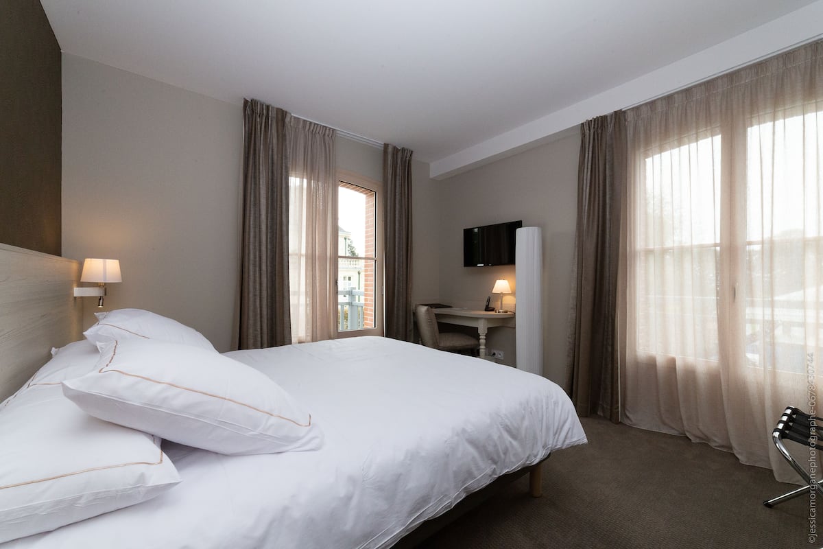 A hotel room with a large bed, a desk, a chair, a TV, and curtains.