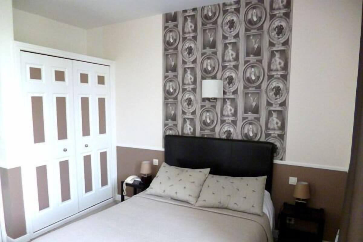 A hotel room with a bed, a nightstand, a lamp, a wardrobe, and a patterned wallpaper.