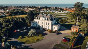 An aerial view of a large, historic mansion with a spacious driveway and multiple parked cars. - Château de la Gressière (La Bernerie-en-Retz)