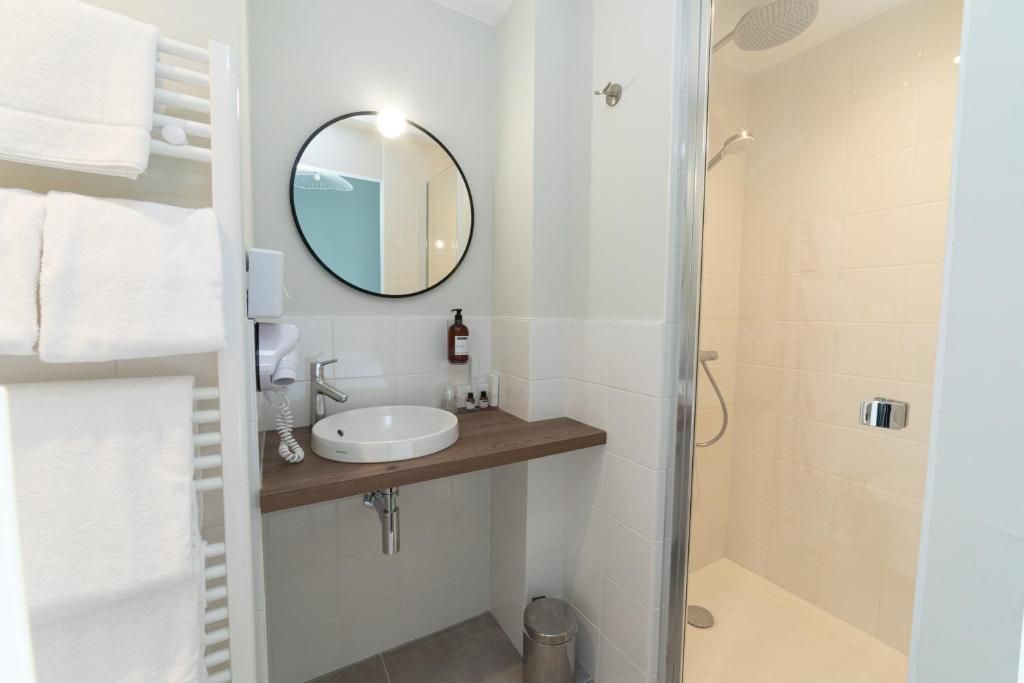 Un baño con lavabo, espejo, toallero y ducha.