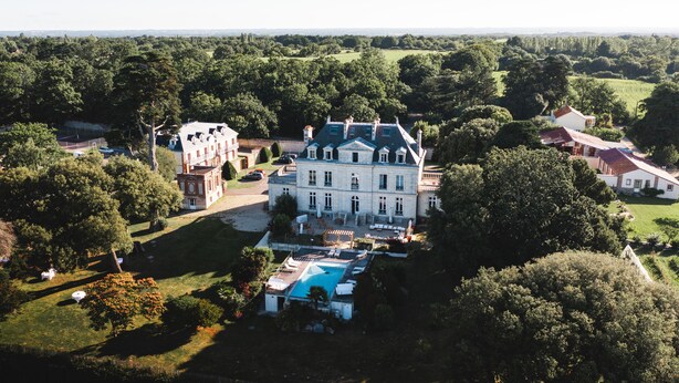 A large, historic mansion with a swimming pool, surrounded by lush greenery and other buildings. - Château de la Gressière (La Bernerie-en-Retz)