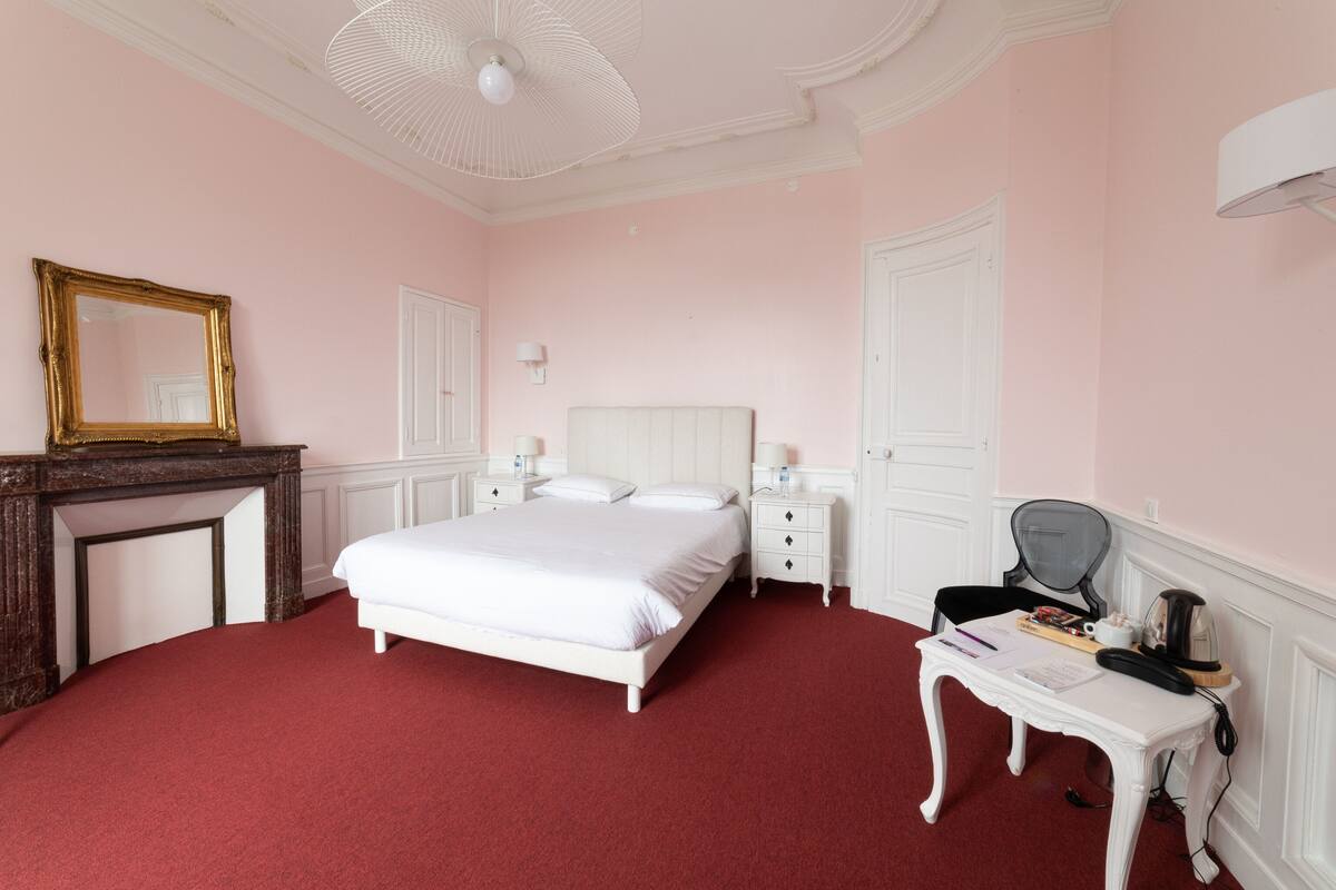 A bedroom with a white bed, a dresser, a desk, and a mirror.
