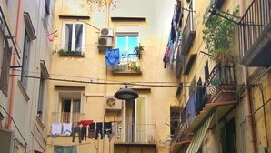 A narrow street with multi-story buildings, balconies with hanging laundry, and parked motorcycles. - Dimora dei Giganti (Naples)
