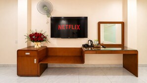 A hotel room with a wooden desk, a television mounted on the wall, a small fan, and a vase of red flowers. - Golden Star Hotel (Ho Chi Minh City)