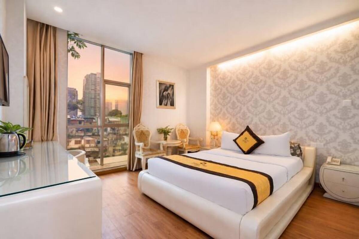 Een hotelkamer met een groot bed, een bureau, een stoel, een bijzettafeltje, een lamp en uitzicht op de skyline.