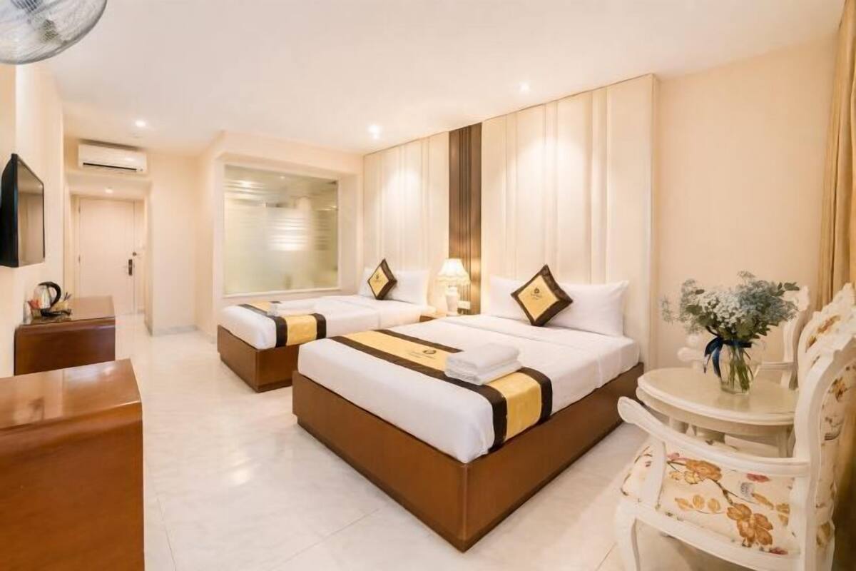 A hotel room with two beds, a desk, a chair, and a small table with a vase.