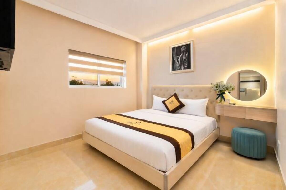 Een hotelkamer met een bed, nachtkastje, spiegel en raam met jaloezieën.