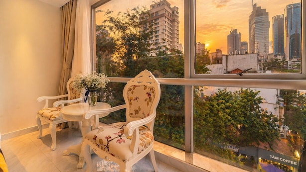 A balcony with two chairs and a small table, a vase of flowers, and a cityscape view at sunset. - Golden Star Hotel (Ho Chi Minh City)