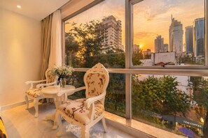 Un balcón con dos sillas, una mesita, un florero y vista a la ciudad al atardecer.