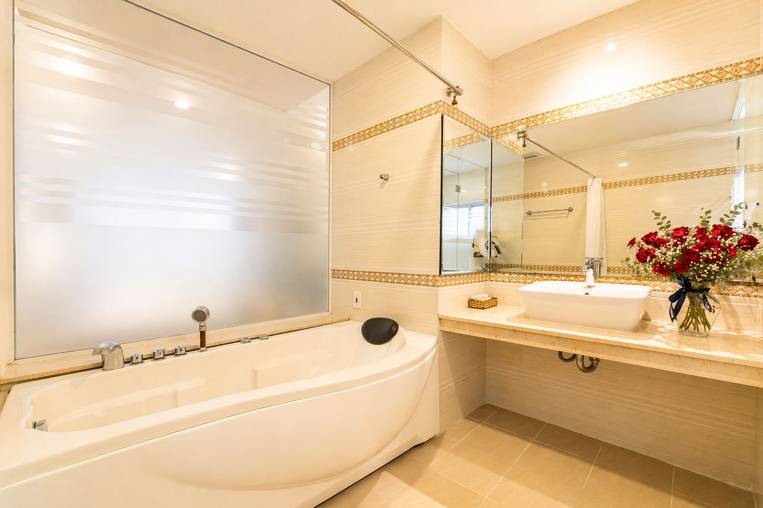 Une salle de bain avec une baignoire, un lavabo, un miroir et un vase de fleurs.