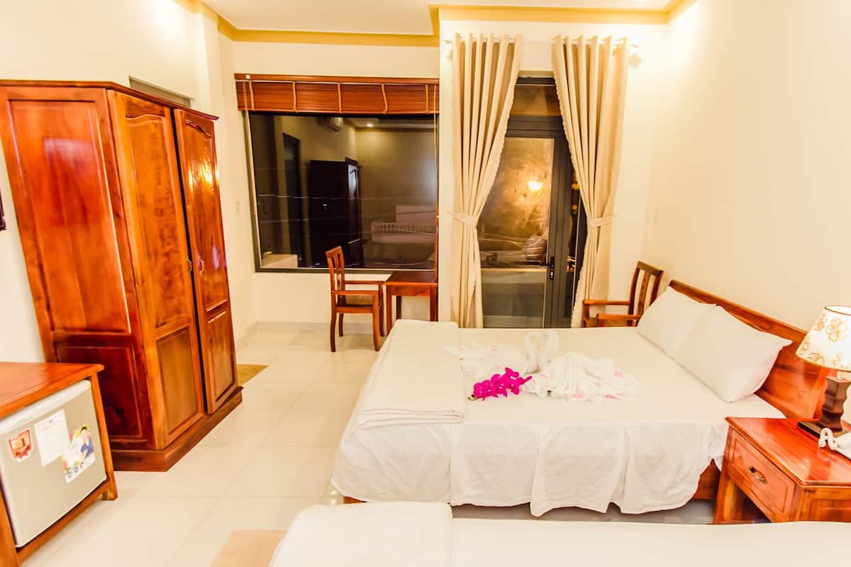 A hotel room with a bed, a desk with a lamp, a wardrobe, and a window with curtains.