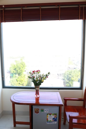 Una stanza con una finestra, un tavolo con un vaso di fiori, un frigorifero e una sedia.