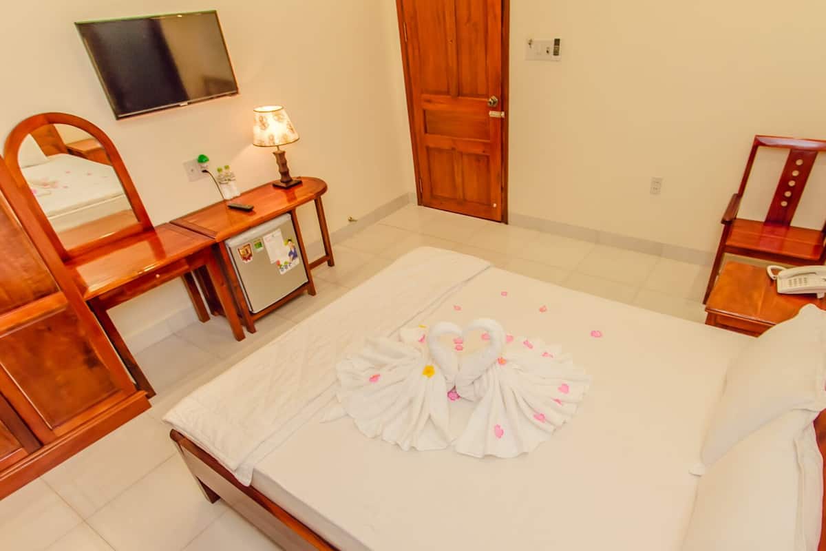 A hotel room with a bed, a desk, a refrigerator, a mirror, a lamp, a phone, and a door.