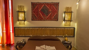 A neatly made bed with a folded towel, a decorative tapestry, and two wall-mounted lamps on either side. - Diletto a Napoli B&B (Naples)