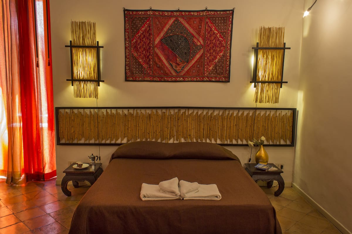 A neatly made bed with a folded towel, a decorative tapestry, and two wall-mounted lamps on either side.