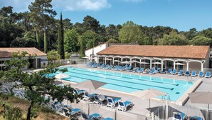 A swimming pool with lounge chairs and umbrellas, surrounded by buildings and trees.