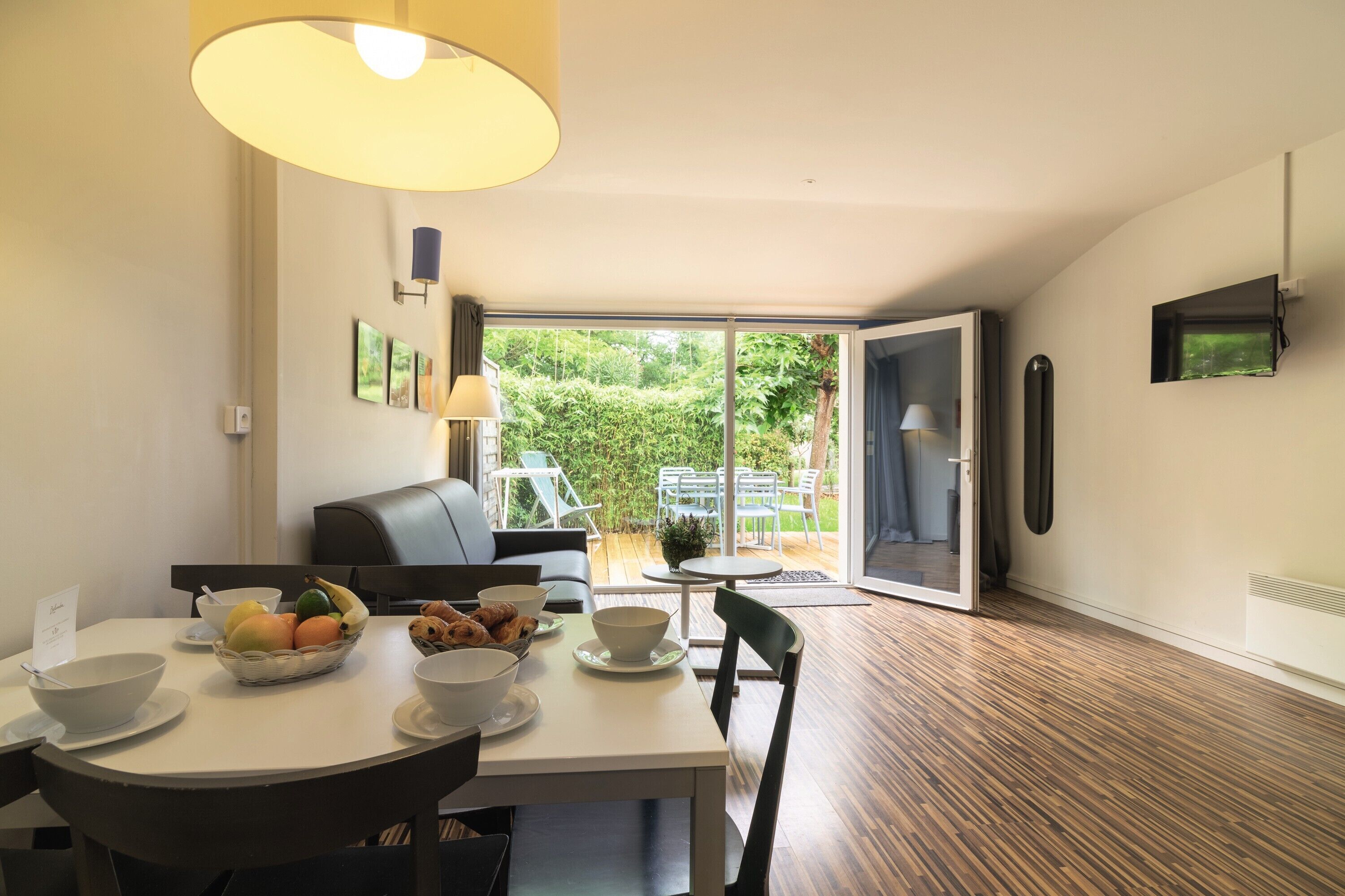 Un coin repas avec une table mise pour le petit-déjeuner, un canapé et une vue sur le jardin grâce à des portes vitrées.