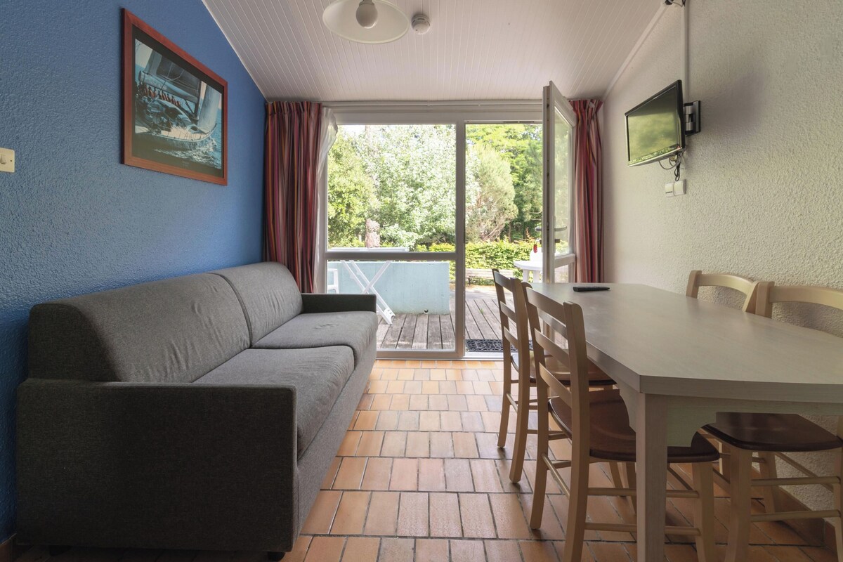 A room with a sofa, a dining table with chairs, a TV mounted on the wall, and a sliding glass door leading to an outdoor area.