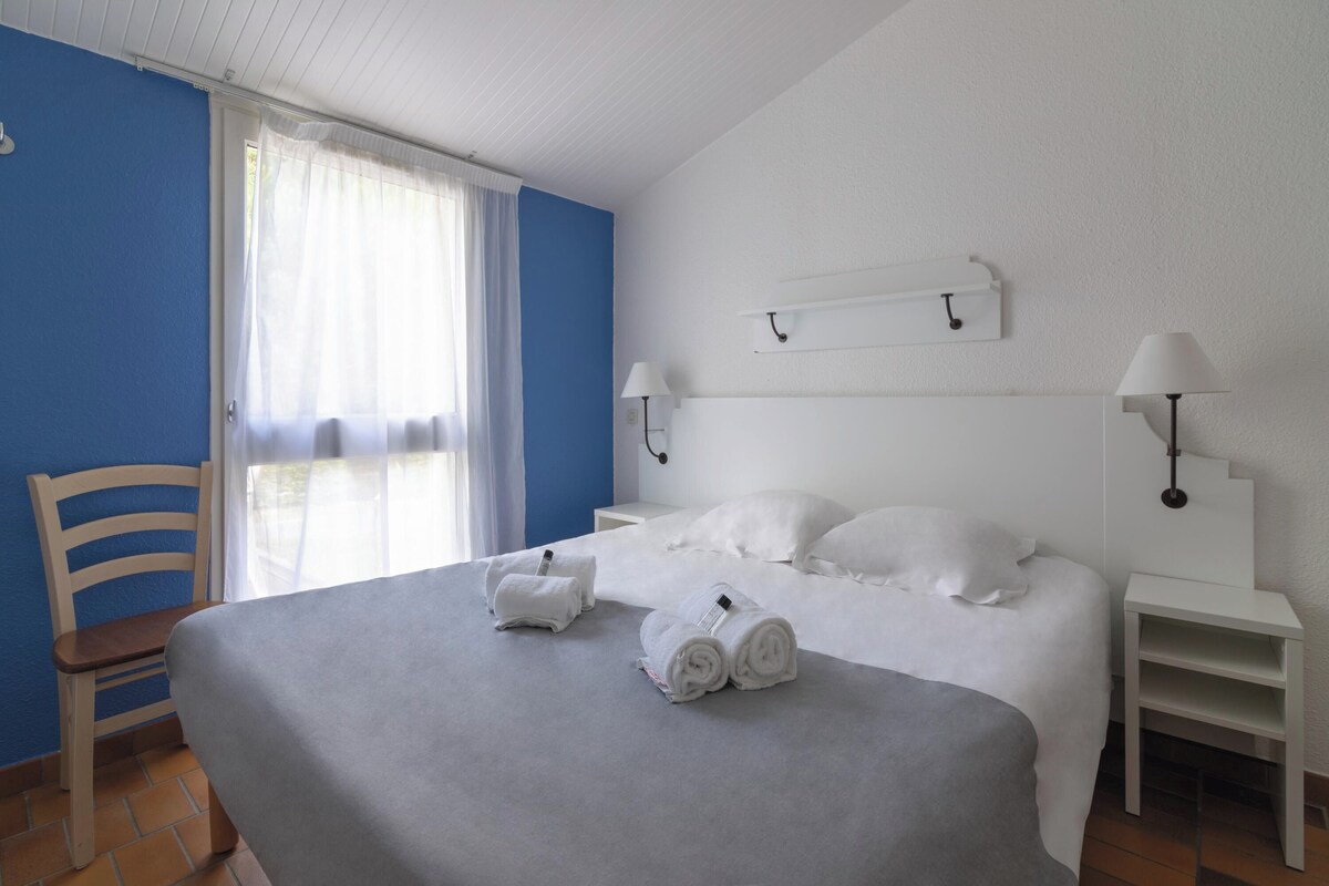 A hotel room with a bed, two bedside tables, a chair, and a window with curtains.