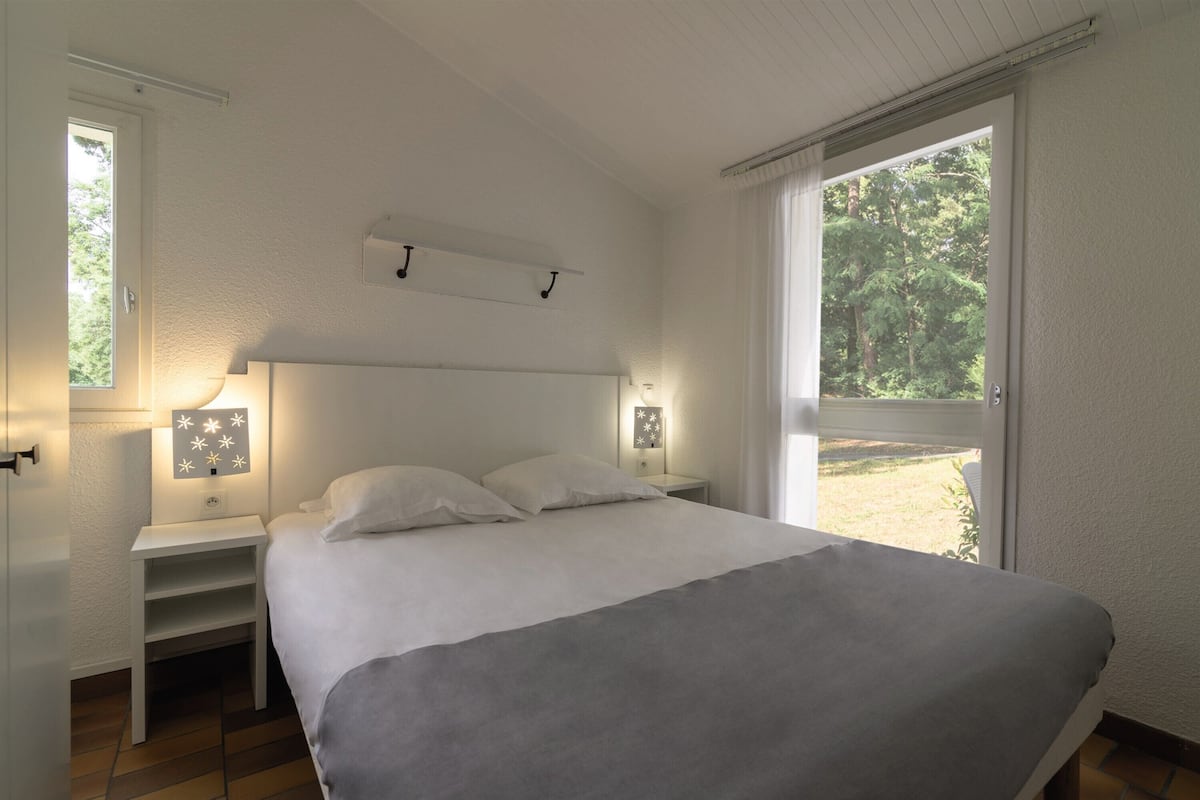 Ein Schlafzimmer mit einem Bett, Nachttischen und einem Fenster mit Blick auf Bäume.