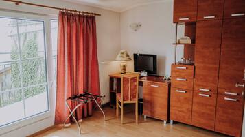 A room with a wooden desk, a chair, a radiator, a TV, and a wardrobe.