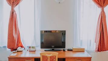 Habitación de hotel con un escritorio de madera, una silla, un televisor y un radiador.