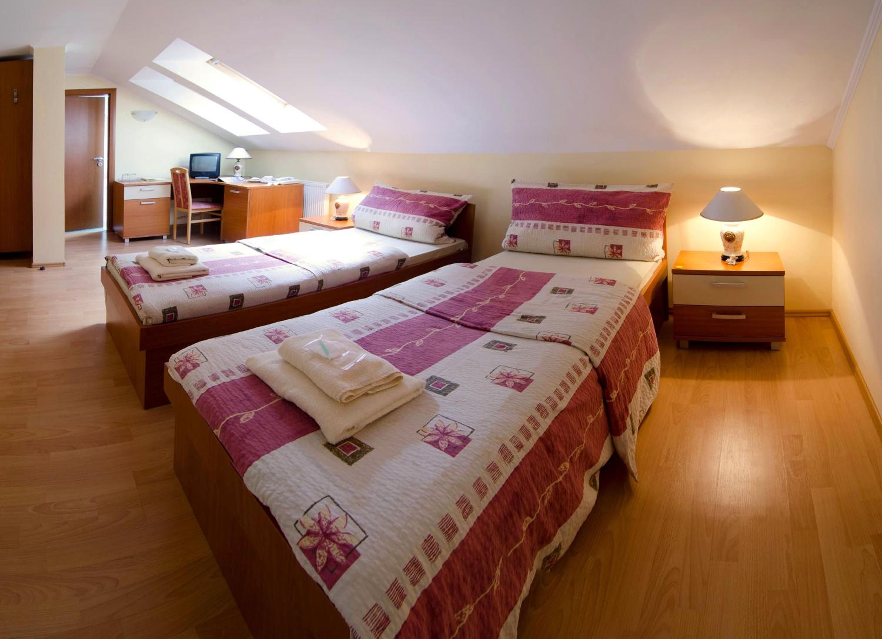 A bedroom with two beds, a desk, a chair, a computer, and a lamp.