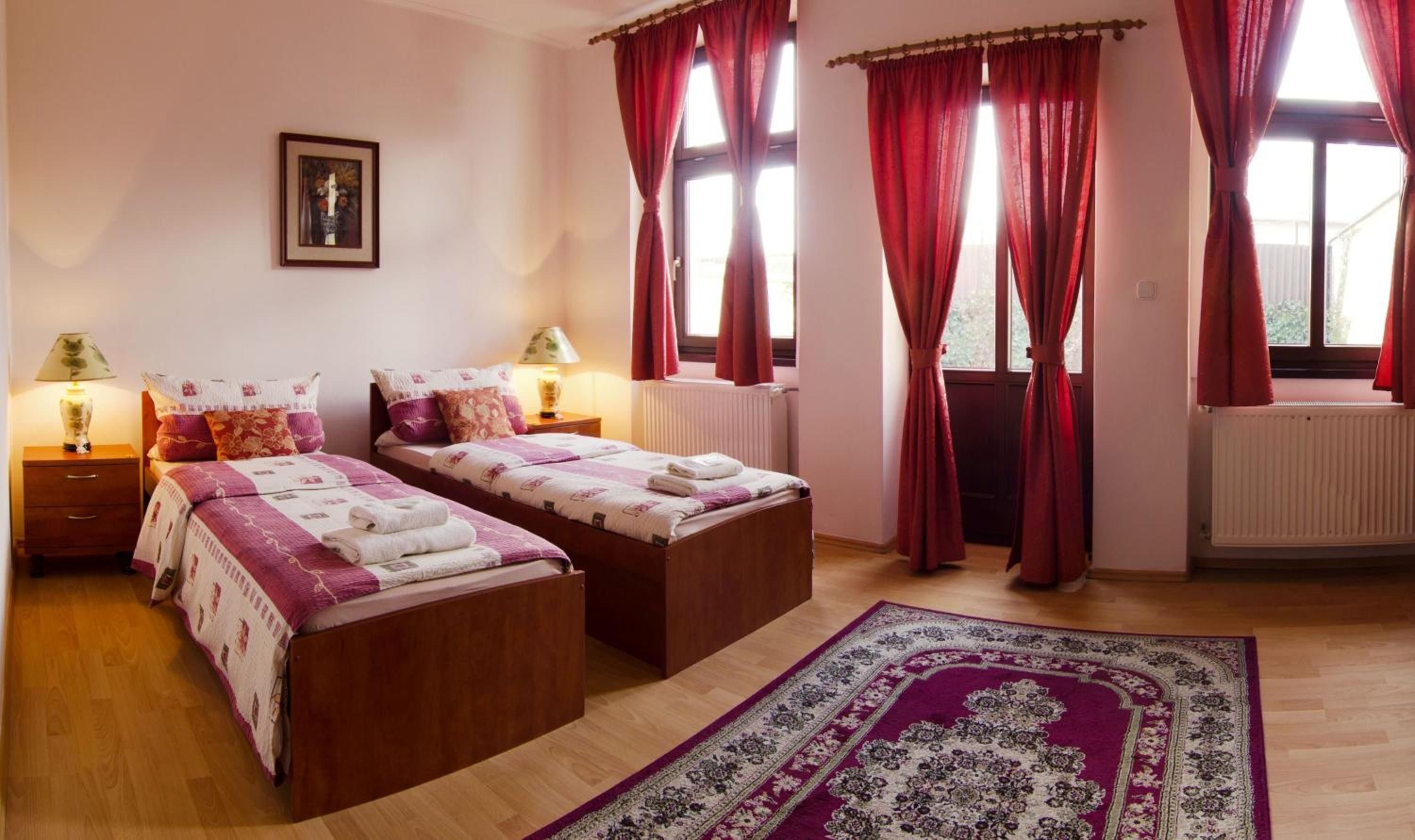Ein Schlafzimmer mit zwei Betten, einem Heizkörper, einem Fenster mit Vorhängen, einem Teppich und einem Bild an der Wand.