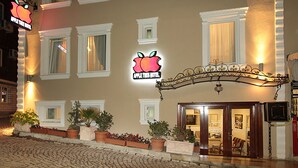 A hotel entrance with a neon apple sign, multiple windows, and potted plants. - Apple Tree Hotel (Istanbul)