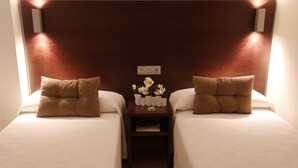 Une chambre d’hôtel avec deux lits, chacun agrémenté d’un oreiller marron et d’une petite table sur laquelle est posé un vase de fleurs, placé entre les deux lits.