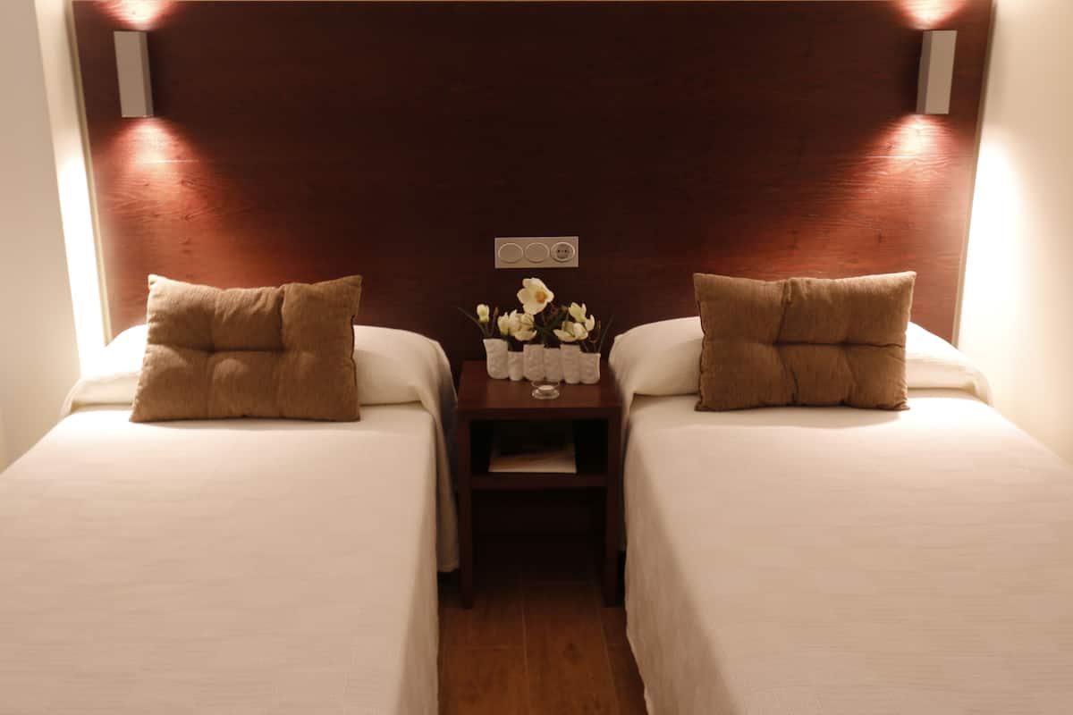 Une chambre d’hôtel avec deux lits, chacun agrémenté d’un oreiller marron et d’une petite table sur laquelle est posé un vase de fleurs, placé entre les deux lits.