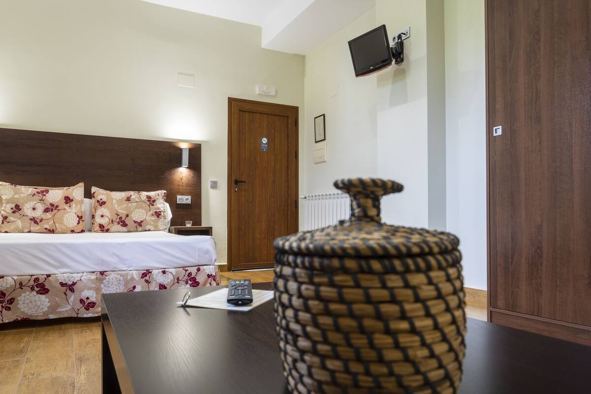 Une chambre d’hôtel comprenant un lit, une table de chevet, un téléviseur fixé au mur et une armoire en bois.