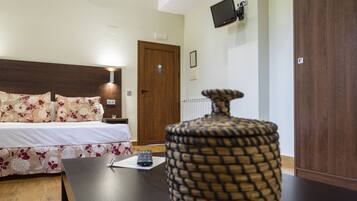 Una habitación de hotel con cama, mesita de noche, televisor montado en la pared y armario de madera.