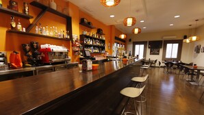 Un espace bar avec un long comptoir, des tabourets, des étagères remplies de bouteilles et un appareil à café.