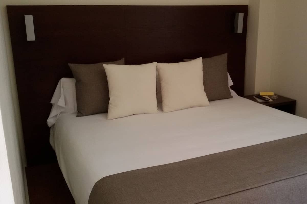 Une chambre d’hôtel avec un grand lit, une tête de lit en bois et une table de chevet avec une télécommande.