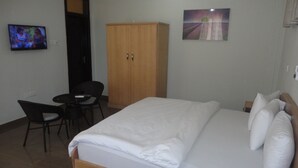 Ett sovrum med en säng, en garderob i trä, en tv och en matplats med en stol och ett bord.