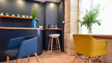 A modern interior with a dark wall, wooden shelves, a blue chair, a yellow chair, and a window with a plant.