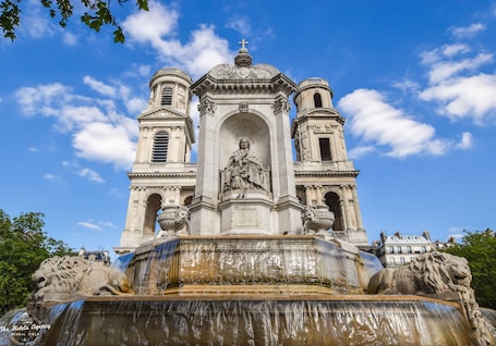 A historic fountain with a statue in the center, surrounded by ornate architecture and two lion statues.