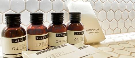 A bathroom with a hexagonal tile backsplash and a white sink area. There are four bottles labeled 'GREEN L' with numbers 01 to 04, and a white packet labeled 'SHOWER CAP'.