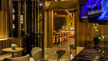 A modern hotel lobby with a bar area, seating, and a television displaying a cityscape.