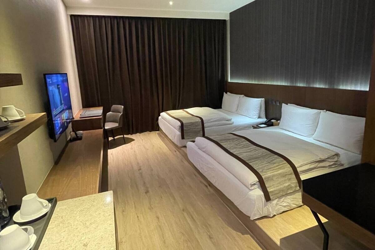 A hotel room with two beds, a desk with a computer, a chair, and a TV.