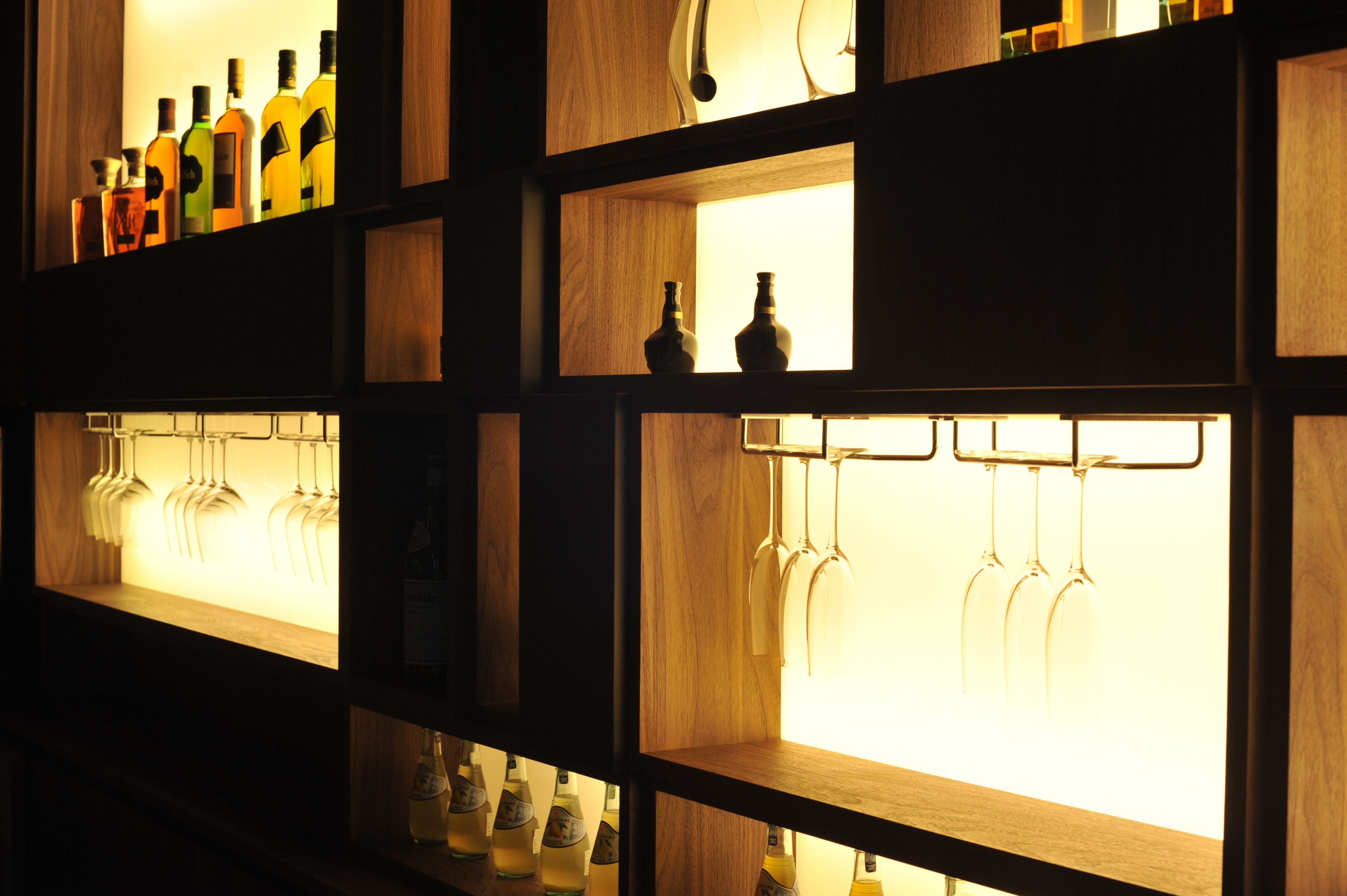 A bar area with shelves holding bottles and wine glasses.