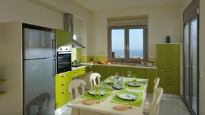 A modern kitchen with a dining area, featuring a stainless steel refrigerator, green cabinets, and a window with a city view.
