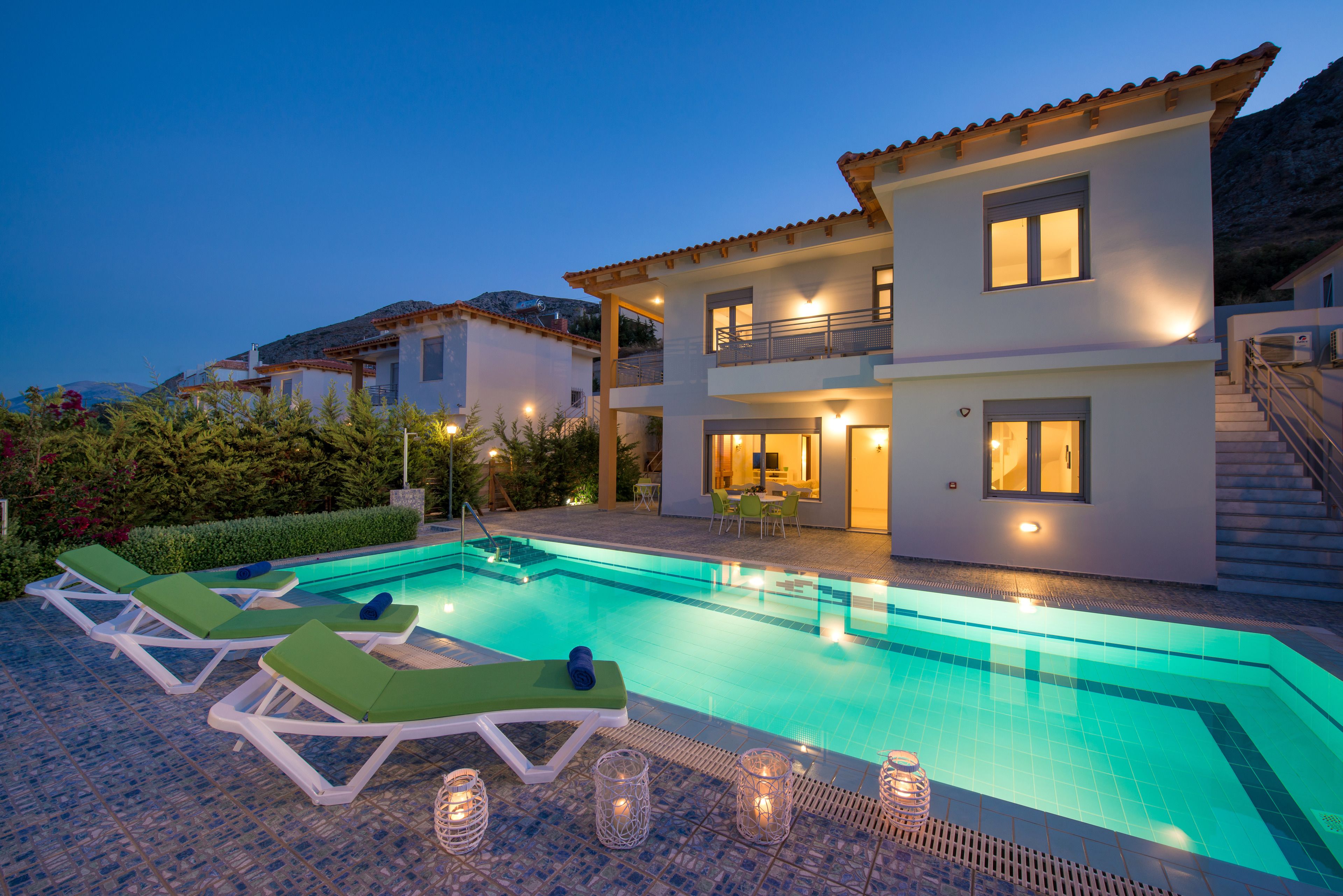 A modern two-story house with a swimming pool, lounge chairs, and a well-lit patio area.