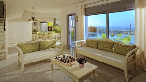 A living room with two sofas, a coffee table with a chessboard, and a view of the city through large windows.