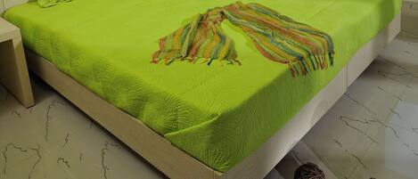 Un lit avec une couvre-lit verte et des oreillers, une table de chevet avec une lampe et une fenêtre avec des rideaux.